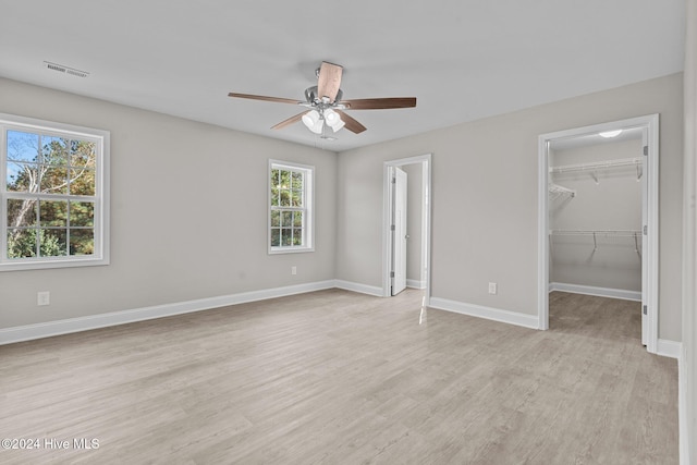 unfurnished bedroom with light hardwood / wood-style floors, a spacious closet, ceiling fan, and a closet