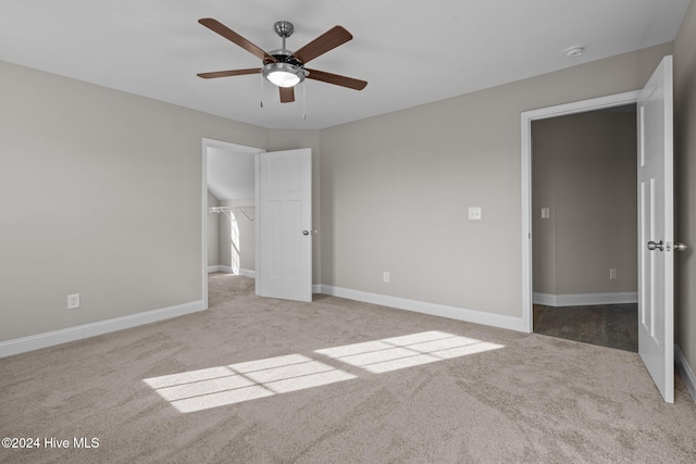 unfurnished bedroom featuring ceiling fan, a closet, a walk in closet, and light colored carpet