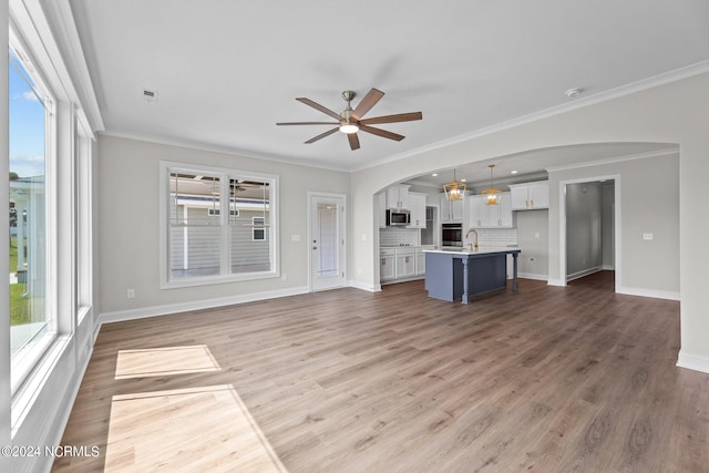 unfurnished living room with light wood-type flooring, ornamental molding, and ceiling fan