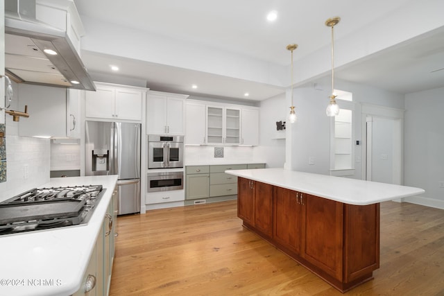 kitchen featuring ventilation hood, stainless steel appliances, white cabinets, a kitchen island, and hanging light fixtures