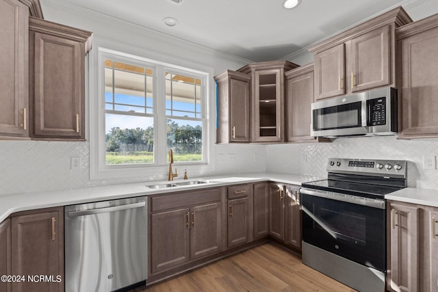 kitchen with hardwood / wood-style floors, backsplash, appliances with stainless steel finishes, ornamental molding, and sink