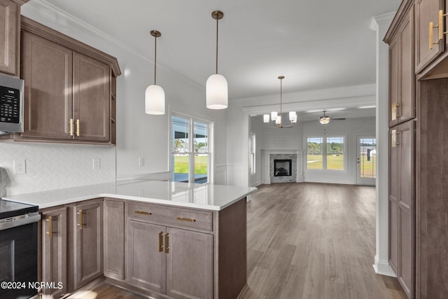 kitchen with a large fireplace, appliances with stainless steel finishes, light hardwood / wood-style floors, kitchen peninsula, and tasteful backsplash