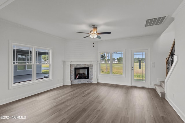 unfurnished living room with ceiling fan, ornamental molding, a stone fireplace, and hardwood / wood-style flooring