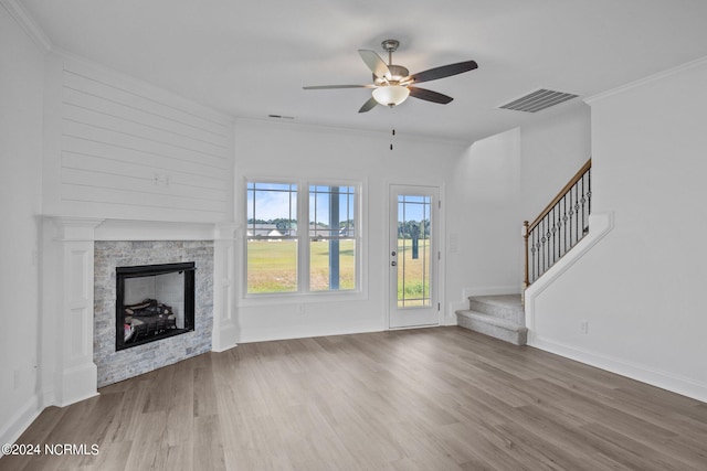 unfurnished living room with ornamental molding, wood-type flooring, ceiling fan, and a stone fireplace