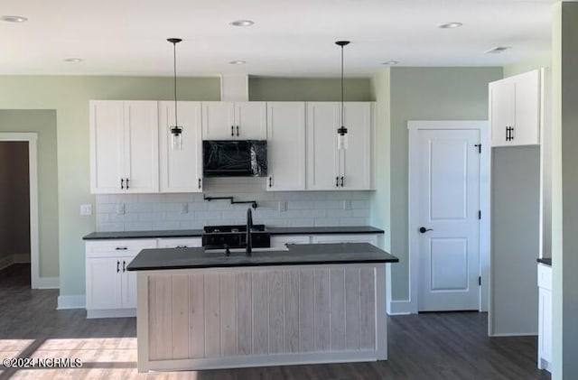 kitchen featuring decorative light fixtures, decorative backsplash, white cabinets, an island with sink, and dark wood-type flooring