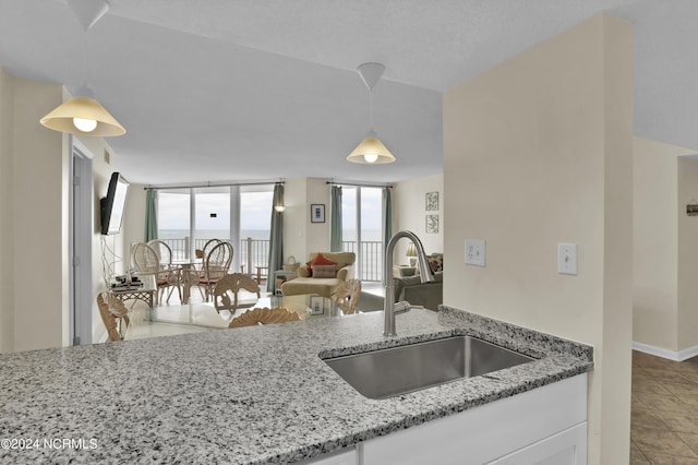 kitchen with sink, a wall of windows, light stone counters, pendant lighting, and white cabinets