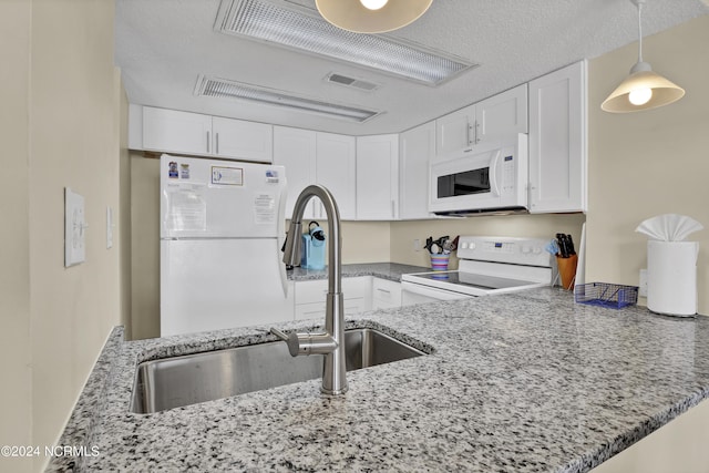 kitchen with white appliances, stone counters, white cabinets, sink, and kitchen peninsula