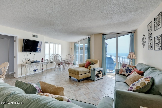 living room with expansive windows, light tile patterned floors, a water view, and a textured ceiling