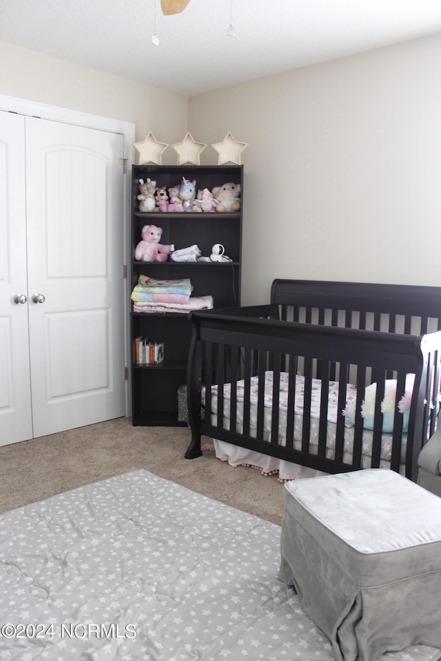 bedroom with a crib, carpet, ceiling fan, and a closet