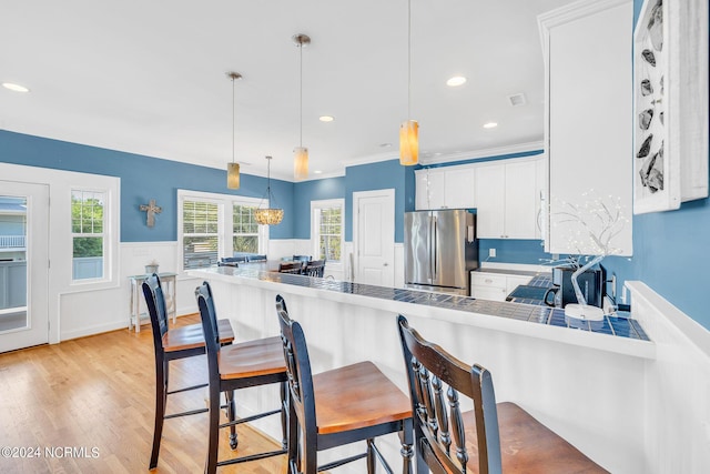 kitchen featuring a kitchen bar, stainless steel fridge, kitchen peninsula, white cabinets, and hanging light fixtures