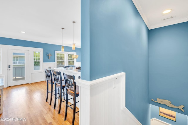 kitchen featuring pendant lighting, a kitchen breakfast bar, light hardwood / wood-style floors, and ornamental molding