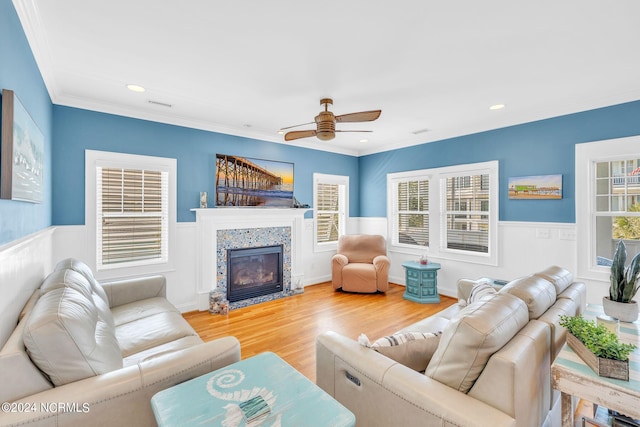 living room featuring hardwood / wood-style floors, ceiling fan, ornamental molding, and a tiled fireplace