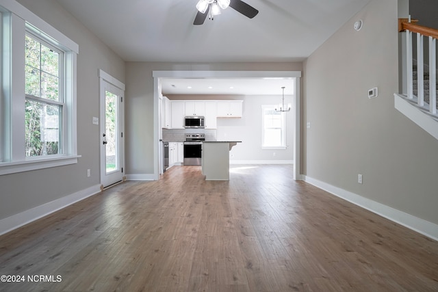 unfurnished living room featuring wood-type flooring and ceiling fan with notable chandelier