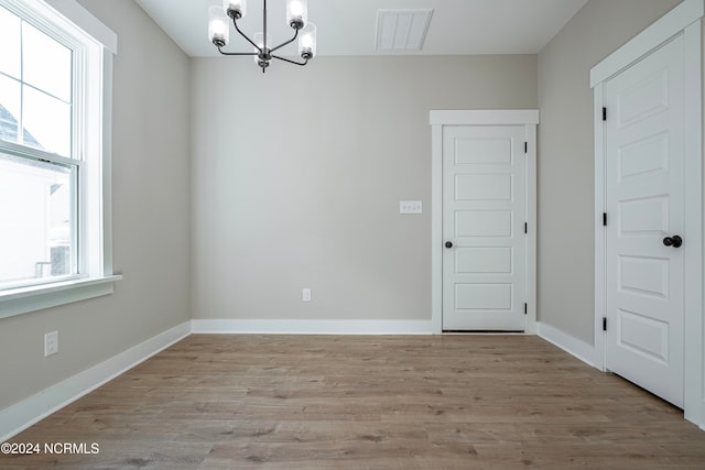 empty room featuring a notable chandelier and light wood-type flooring