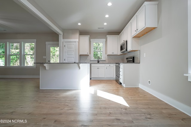 kitchen featuring white cabinetry, stainless steel appliances, light hardwood / wood-style flooring, and a kitchen breakfast bar