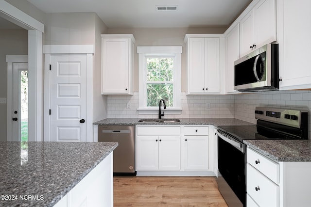 kitchen with dark stone countertops, sink, white cabinets, appliances with stainless steel finishes, and light hardwood / wood-style floors