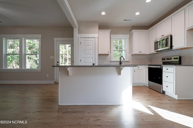 kitchen with white cabinets, dark stone countertops, stainless steel appliances, and a kitchen island