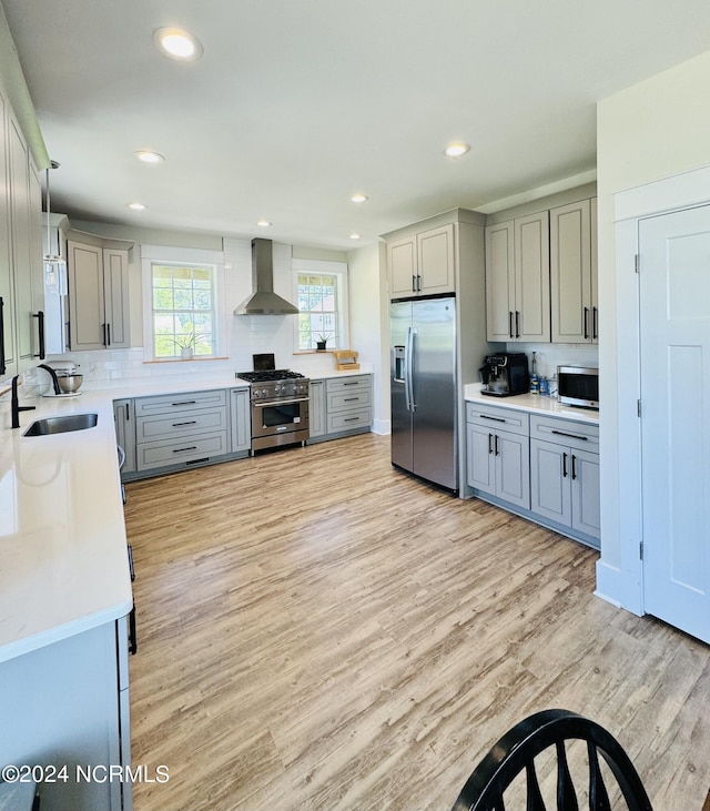 kitchen featuring light wood-type flooring, stainless steel appliances, wall chimney range hood, sink, and decorative light fixtures