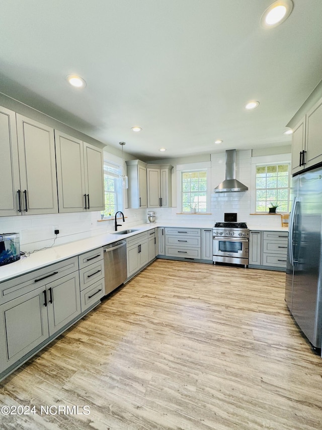 kitchen featuring sink, wall chimney exhaust hood, a healthy amount of sunlight, stainless steel appliances, and decorative light fixtures