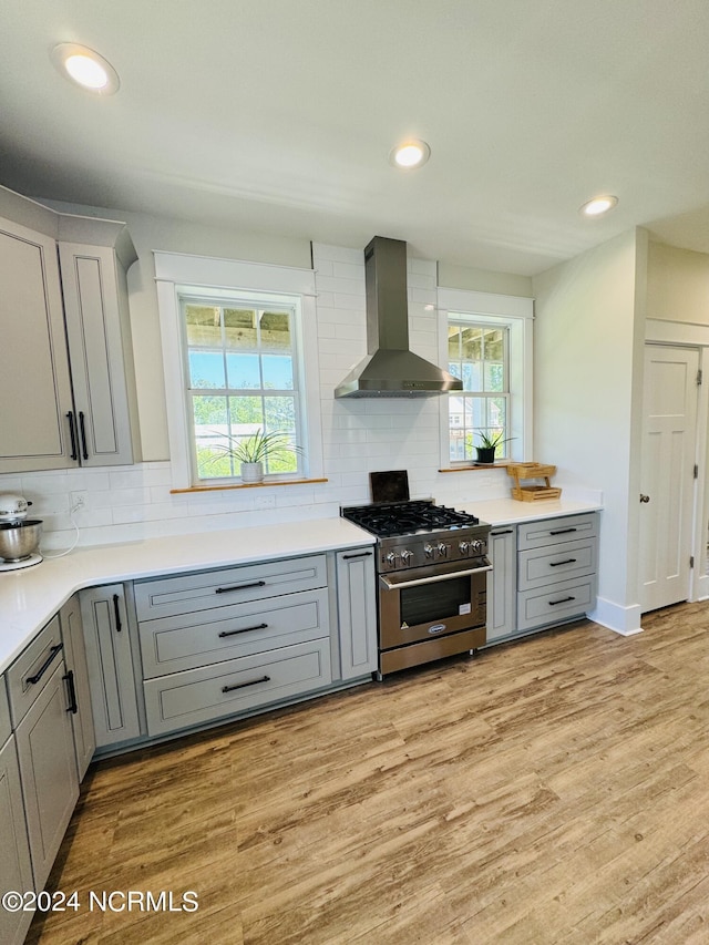 kitchen with light wood-type flooring, high end stove, backsplash, and wall chimney range hood