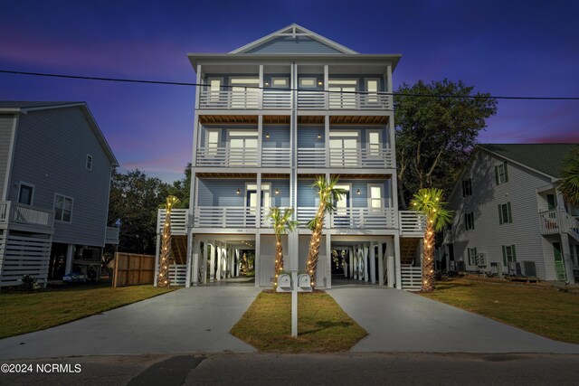 coastal inspired home with a lawn, central air condition unit, a balcony, and a carport