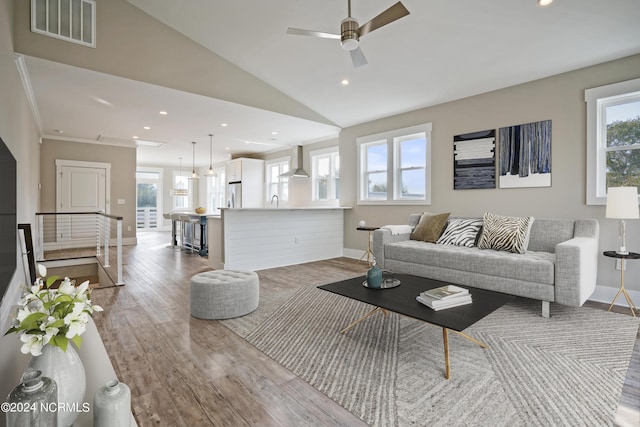 living room with ornamental molding, hardwood / wood-style flooring, vaulted ceiling, and a healthy amount of sunlight