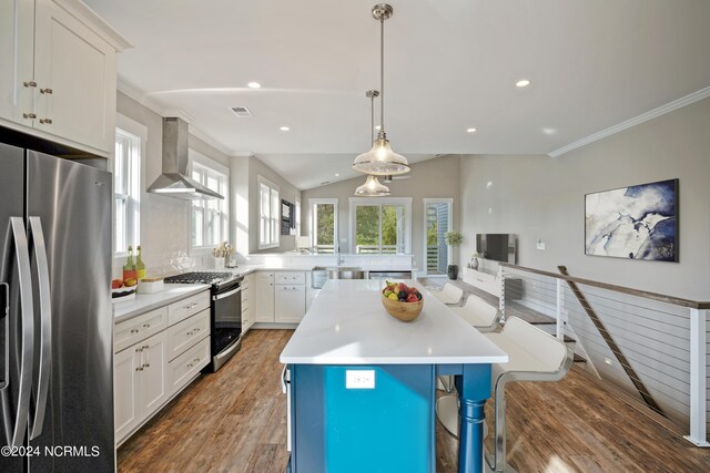 kitchen featuring wall chimney range hood, a kitchen island, stainless steel appliances, hardwood / wood-style flooring, and pendant lighting