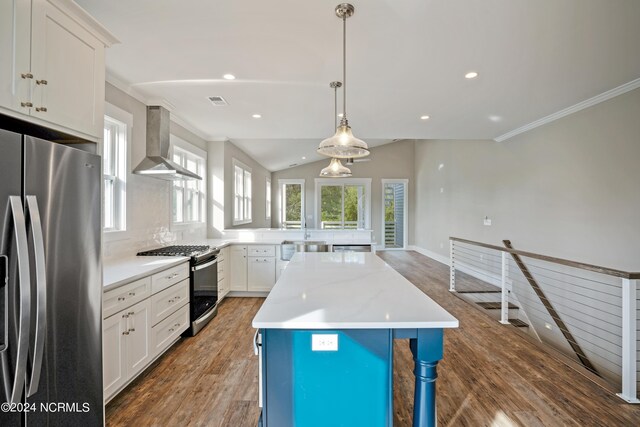 kitchen with a kitchen island, stainless steel appliances, hardwood / wood-style floors, wall chimney exhaust hood, and pendant lighting