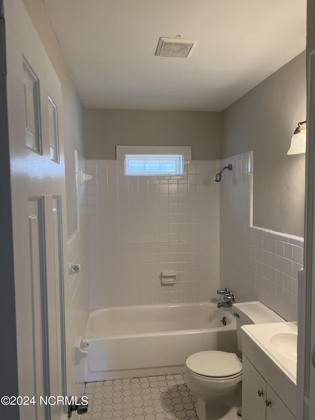 bathroom featuring toilet, vanity, visible vents, tile walls, and  shower combination