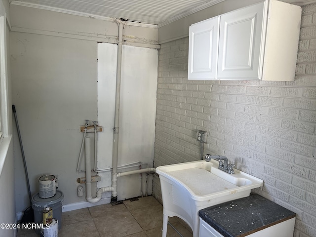 bathroom featuring a sink, brick wall, and tile patterned flooring