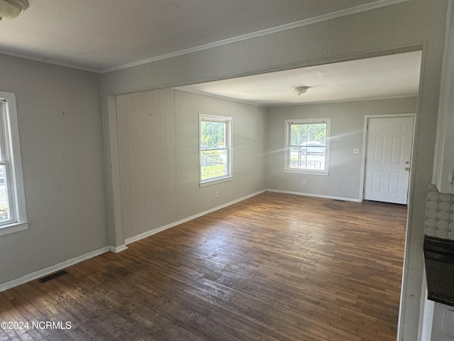 empty room with dark wood-style floors, baseboards, visible vents, and crown molding