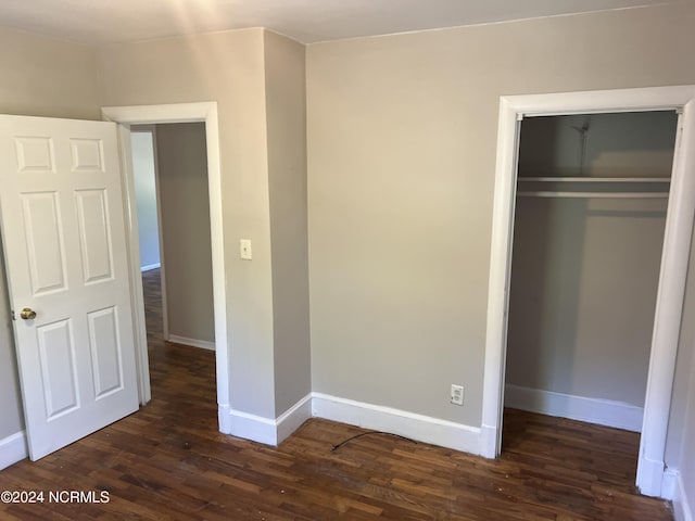 unfurnished bedroom featuring dark wood-type flooring, a closet, and baseboards