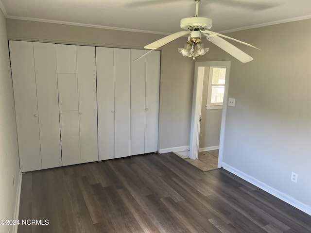 unfurnished bedroom with baseboards, dark wood finished floors, a ceiling fan, ornamental molding, and a closet