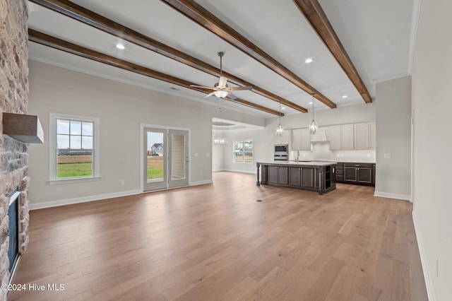 unfurnished living room featuring beam ceiling, ceiling fan, sink, a fireplace, and light wood-type flooring