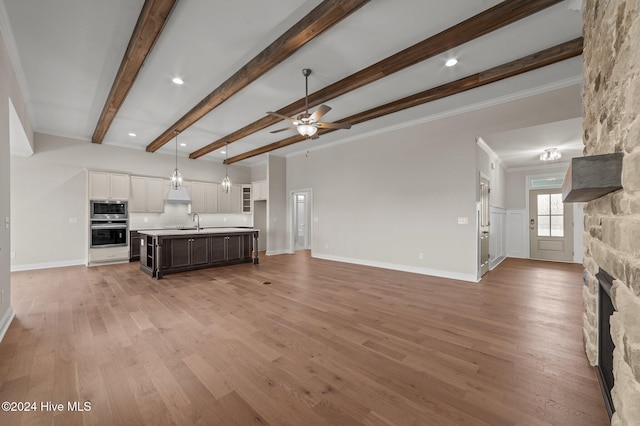 unfurnished living room featuring a stone fireplace, ceiling fan, sink, and hardwood / wood-style floors