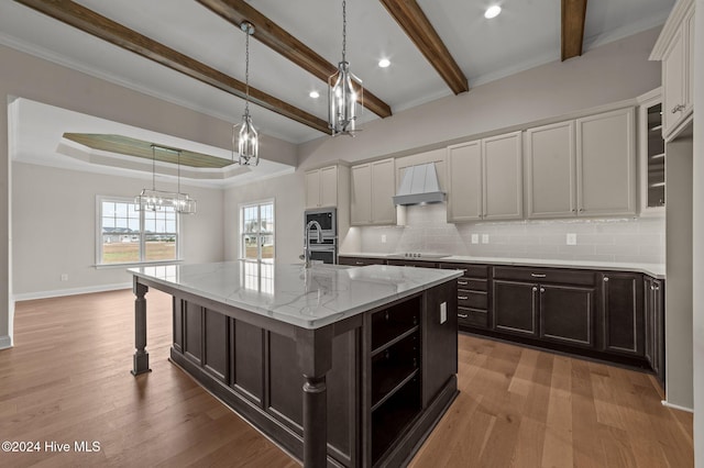 kitchen featuring custom exhaust hood, an island with sink, stovetop, light stone counters, and white cabinetry