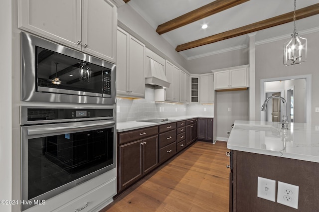 kitchen featuring stainless steel microwave, black electric cooktop, custom range hood, beam ceiling, and white cabinetry