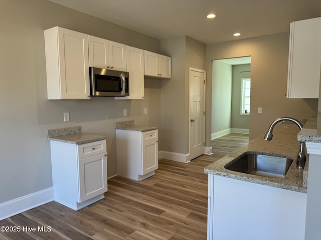 kitchen featuring sink, hardwood / wood-style floors, white cabinets, and light stone counters