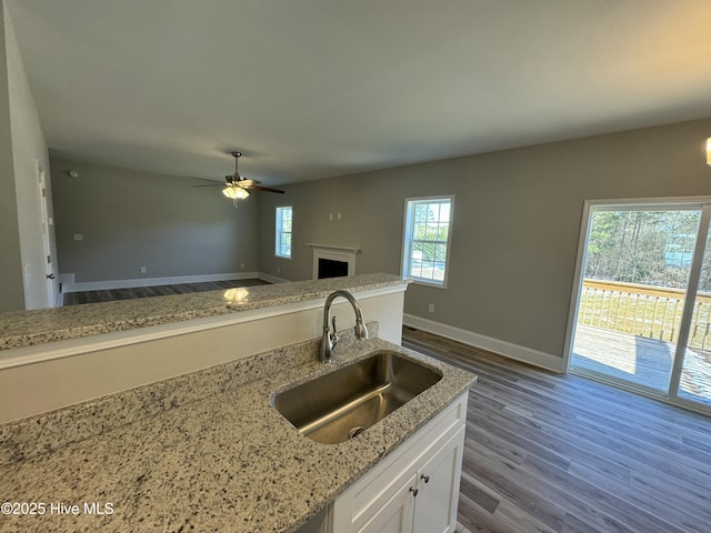 kitchen featuring light stone countertops, white cabinets, dark hardwood / wood-style flooring, sink, and ceiling fan