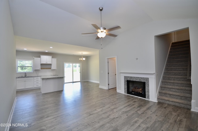 unfurnished living room with ceiling fan with notable chandelier, a sink, wood finished floors, stairs, and vaulted ceiling