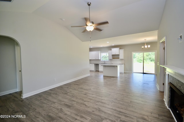 unfurnished living room with ceiling fan with notable chandelier, a fireplace, a sink, wood finished floors, and vaulted ceiling