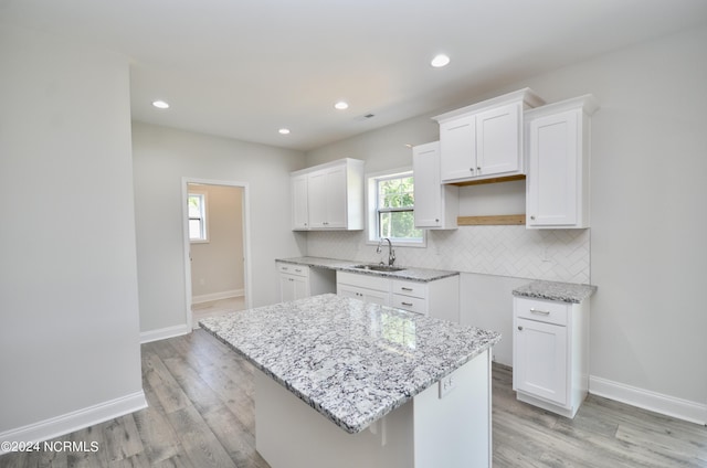 kitchen featuring tasteful backsplash, white cabinets, a sink, light stone countertops, and baseboards