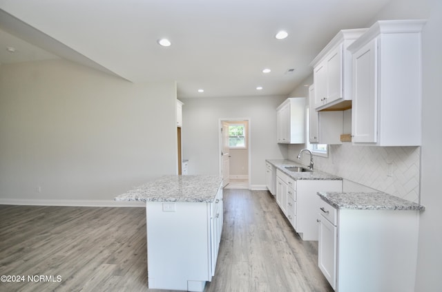 kitchen with light stone counters, light wood-style flooring, a sink, baseboards, and decorative backsplash