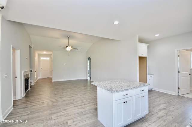 kitchen featuring light wood-style floors, arched walkways, white cabinets, and vaulted ceiling