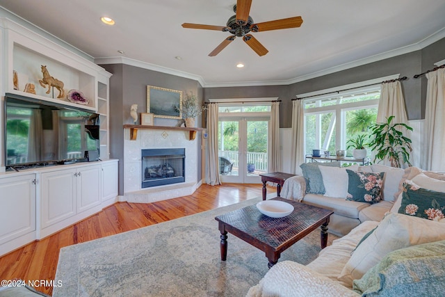 living room featuring a tile fireplace, light hardwood / wood-style flooring, ceiling fan, and ornamental molding