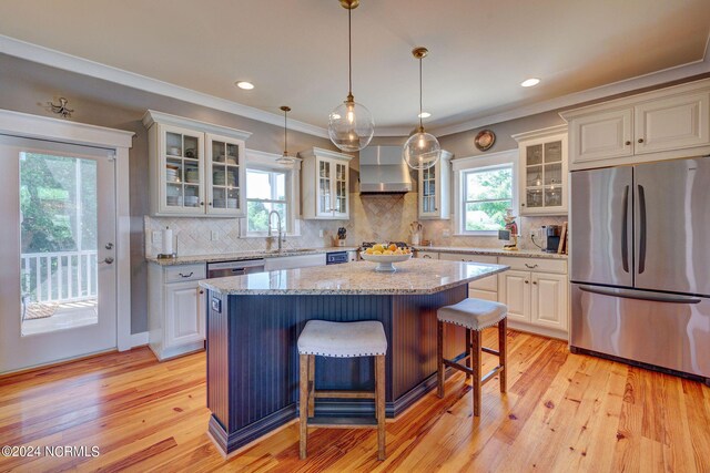 kitchen with light stone counters, a center island, wall chimney range hood, and appliances with stainless steel finishes