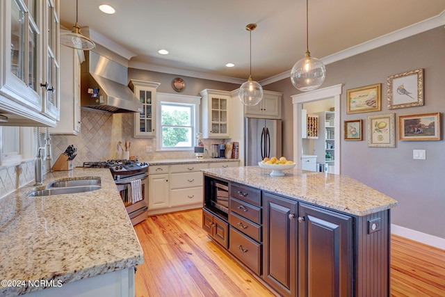 kitchen featuring wall chimney exhaust hood, stainless steel appliances, sink, white cabinets, and a center island