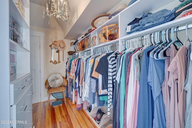 spacious closet with hardwood / wood-style floors, an inviting chandelier, and vaulted ceiling