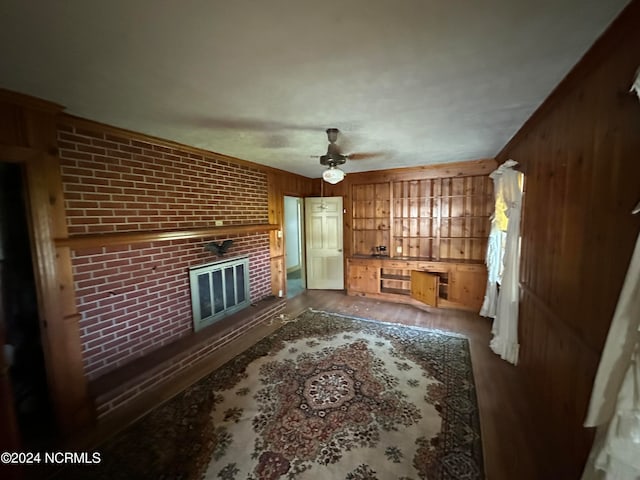 living room with hardwood / wood-style floors, ceiling fan, wooden walls, and a brick fireplace