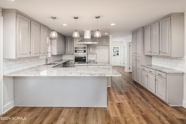 kitchen featuring wall chimney exhaust hood, hardwood / wood-style flooring, hanging light fixtures, and kitchen peninsula